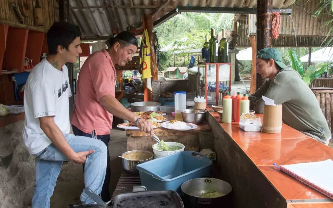 Two you men chat as a third man plates a delicious looking lunch.